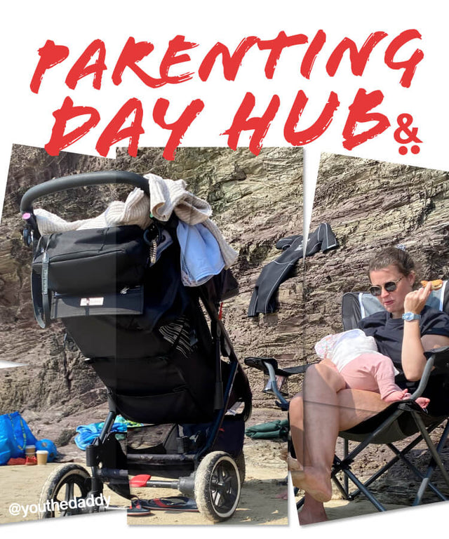 Mum sitting on a chair at the beach feeding baby with a 3 wheel stroller in the foreground - parenting day hub -  philandteds.com